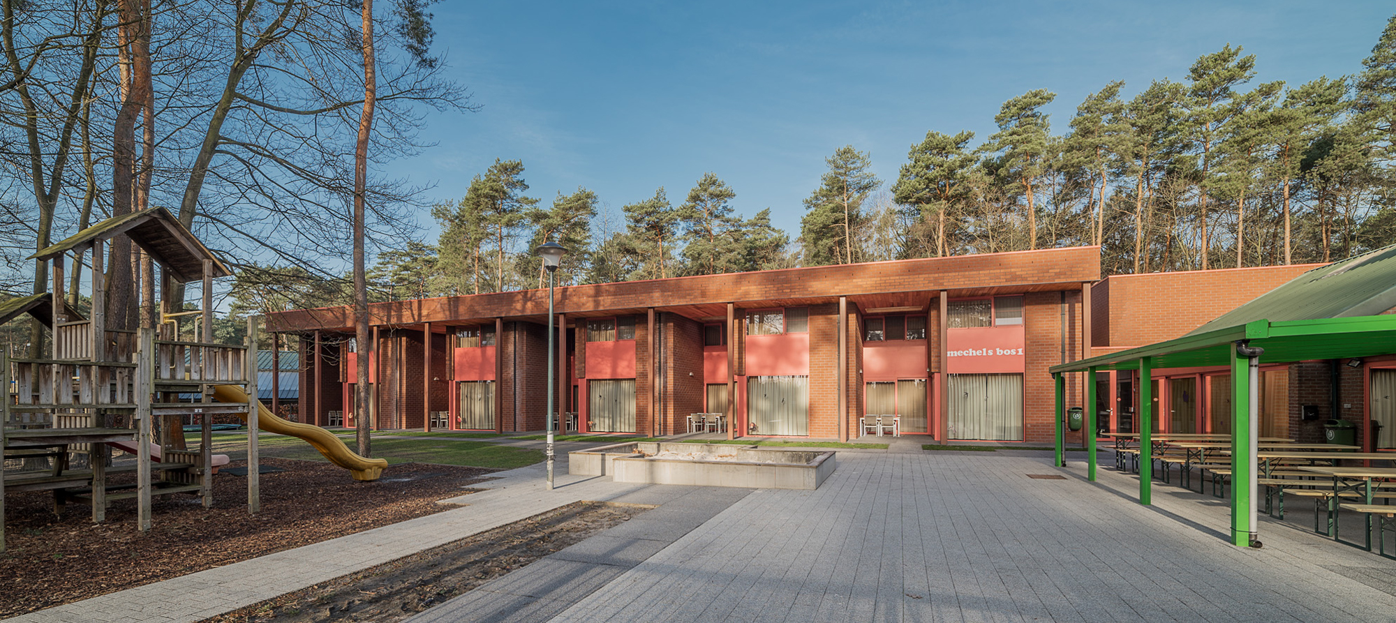 foto van oranje gebouw met bomen op de achtergrond en speeltoestel in de voorgrond