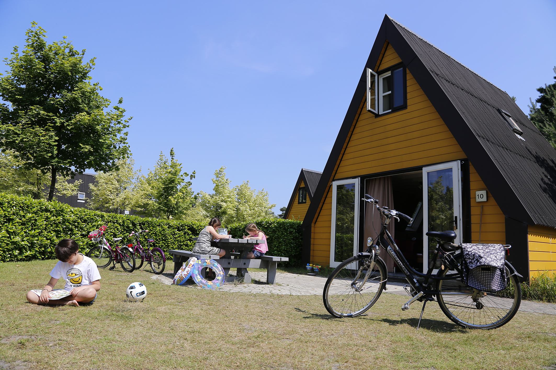 kinderen aan het spelen voor een blokhut, er staat ook een fiets op het grasveld