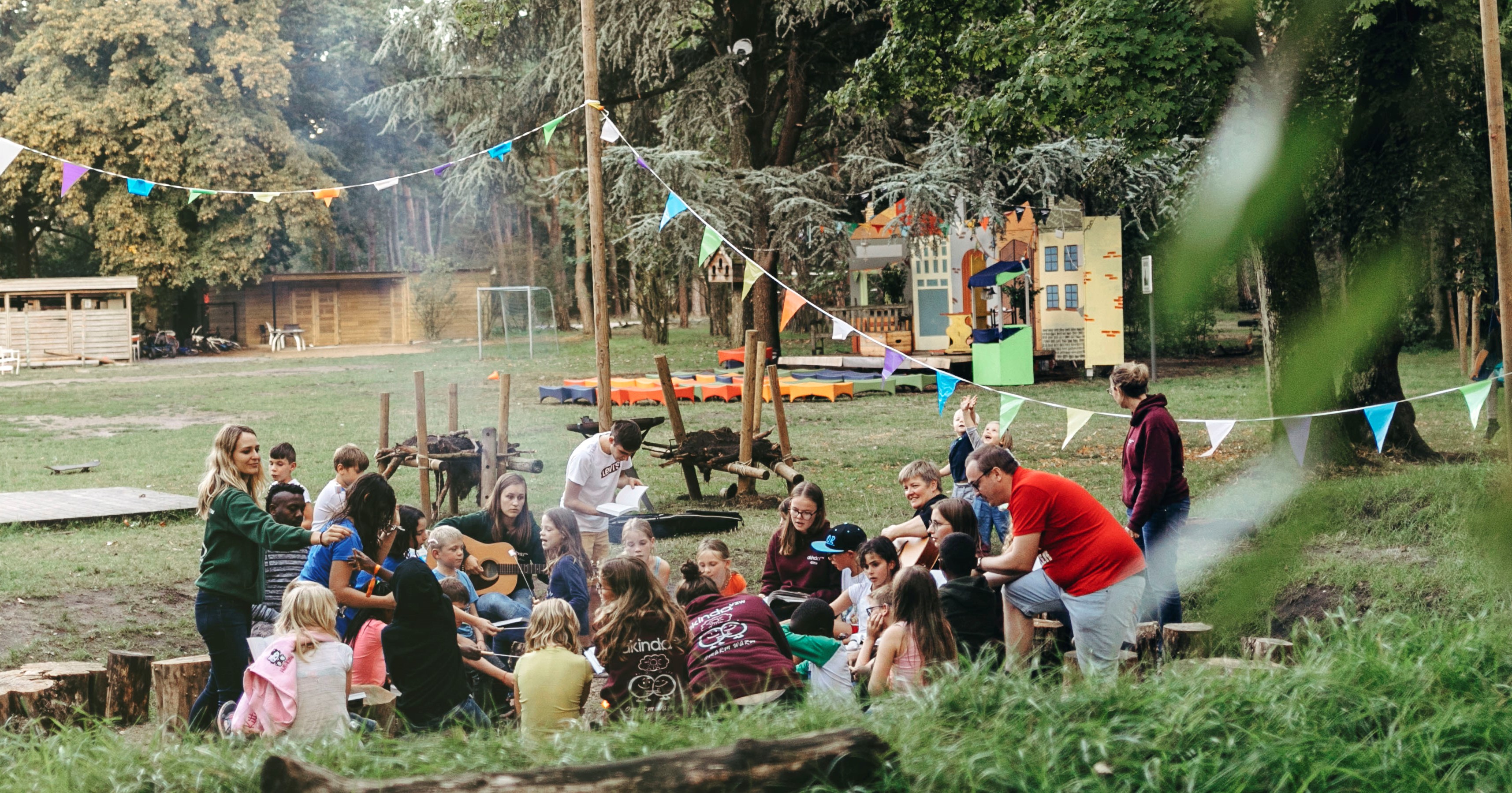 groep jongeren en volwassenen rond kampvuur in open lucht