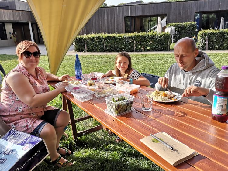 mama dochter en papa die rond een tafel buiten barbecue zitten te eten