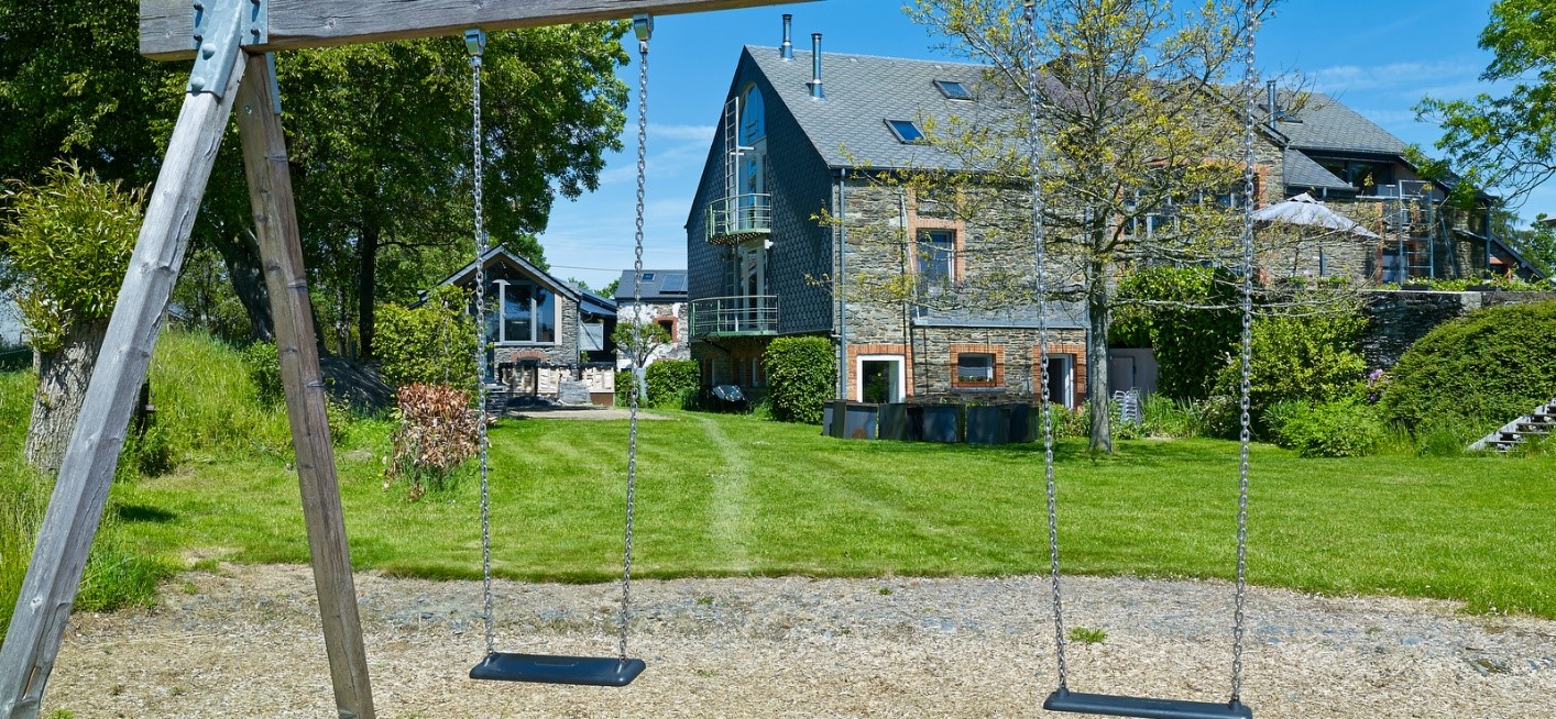 foto van schommel met op de achtergrond een grasveld en een groot vakantiehuis